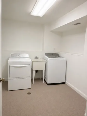 Laundry room featuring neutral carpeting, a utility sink, and overhead fluorescent lighting