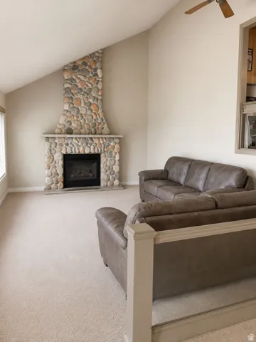 Living area featuring an angled stone fireplace with a black firebox, vaulted ceiling, and neutral-toned carpeting