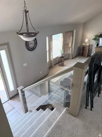 Vaulted ceiling with an attached pendant light fixture, carpeted stairs with a glass and wood-finish railing, bay windows, and a frosted glass-paneled entry door