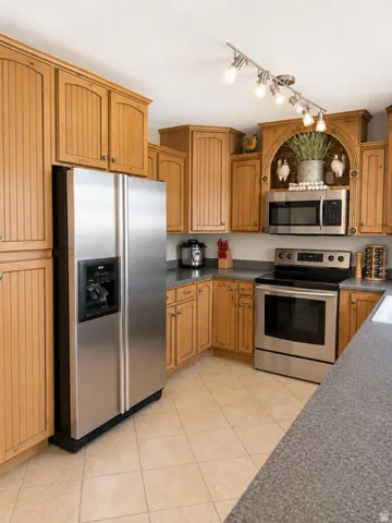 Kitchen featuring light wood cabinetry, stainless steel appliances, speckled gray countertops, and tiled flooring