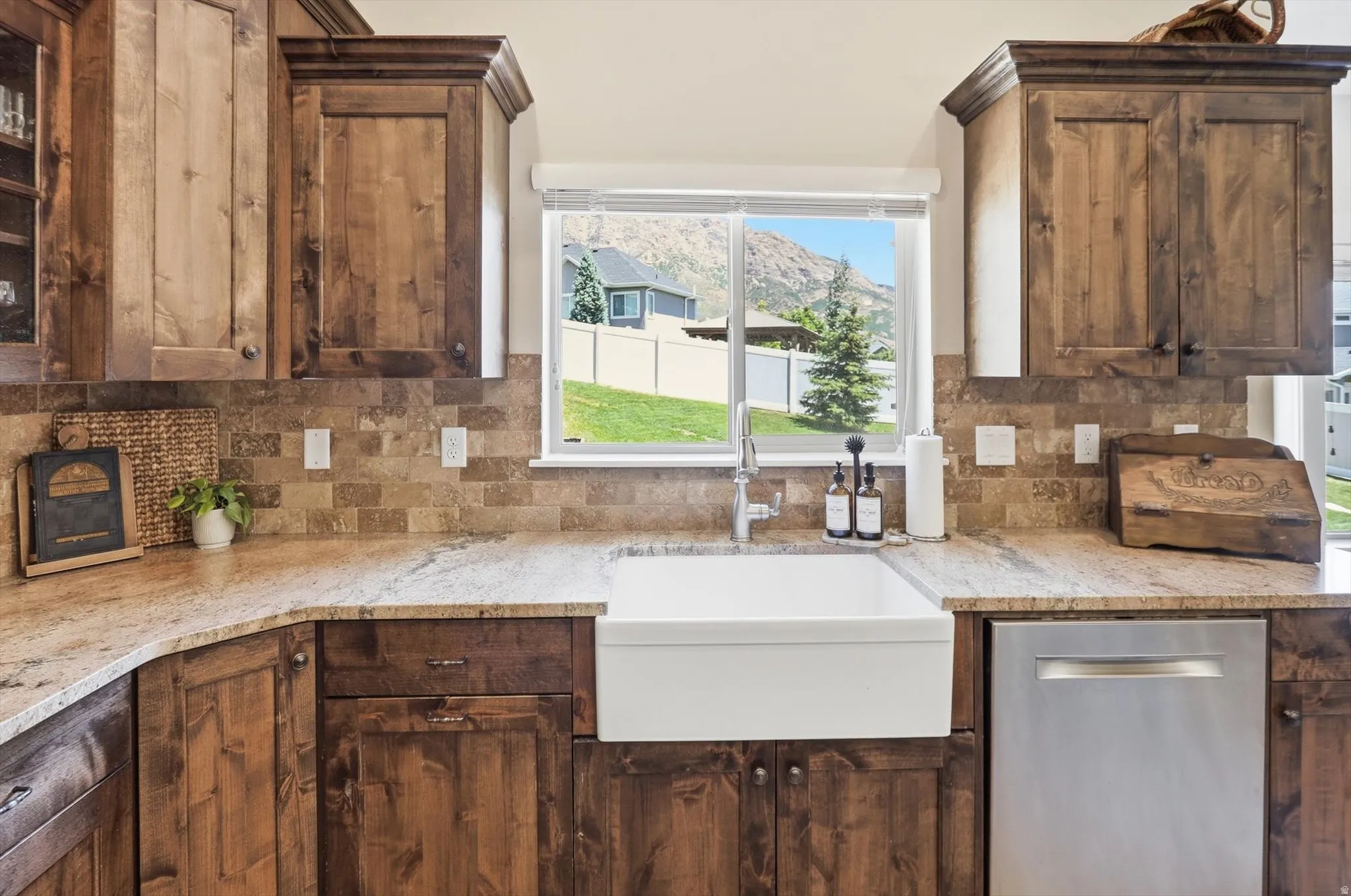 Kitchen featuring wood cabinetry, light-toned countertops, a white farmhouse sink, and a stainless steel dishwasher