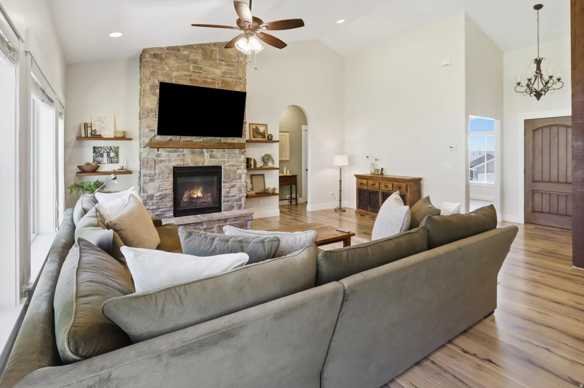 Vaulted living area featuring a stone-clad fireplace with a built-in television, wood-finish flooring, and exposed wood shelving