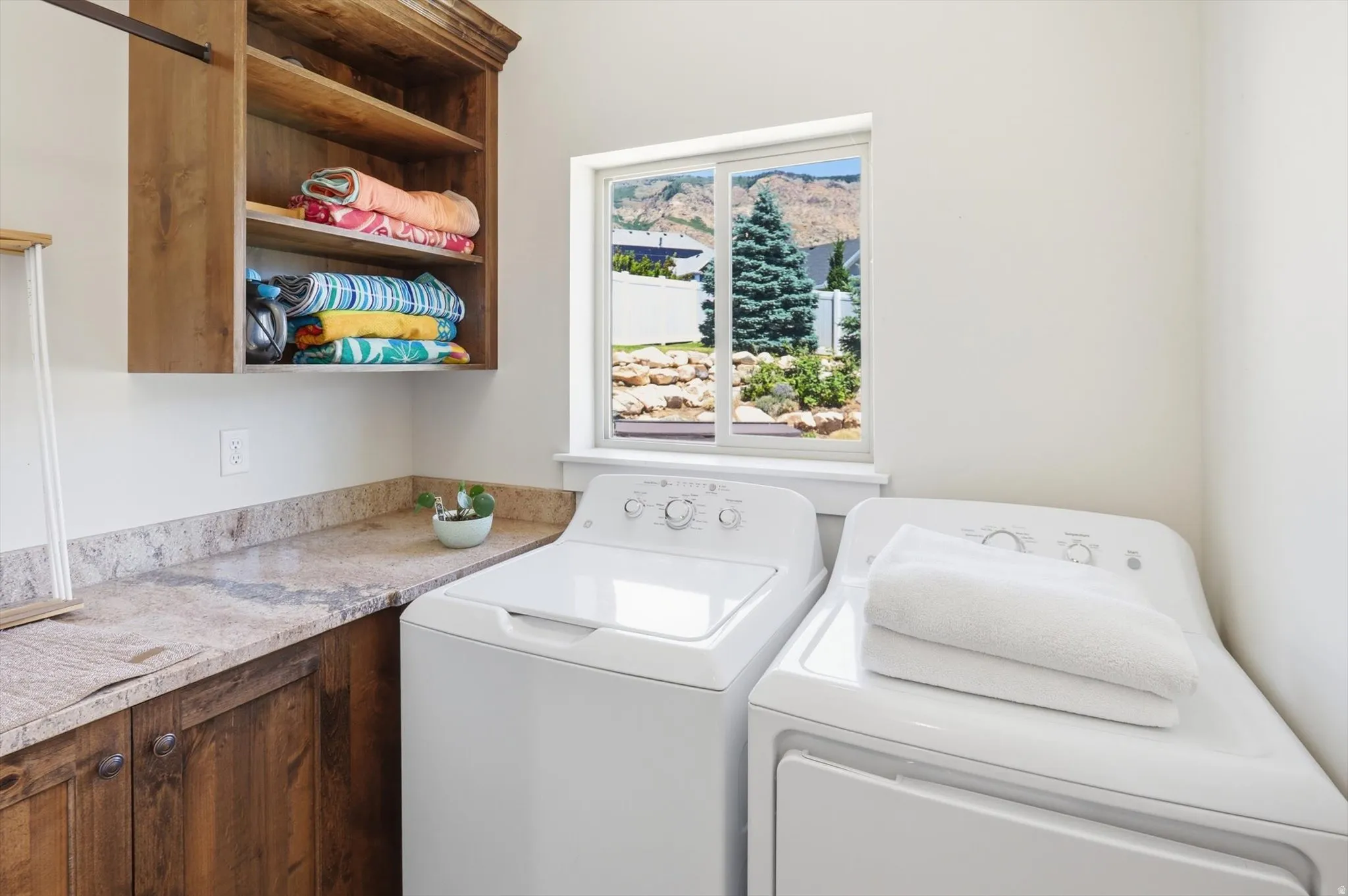 Laundry room featuring an upper wood-finish cabinet with shelving, lower wood-finish cabinetry, and a light-toned patterned countertop