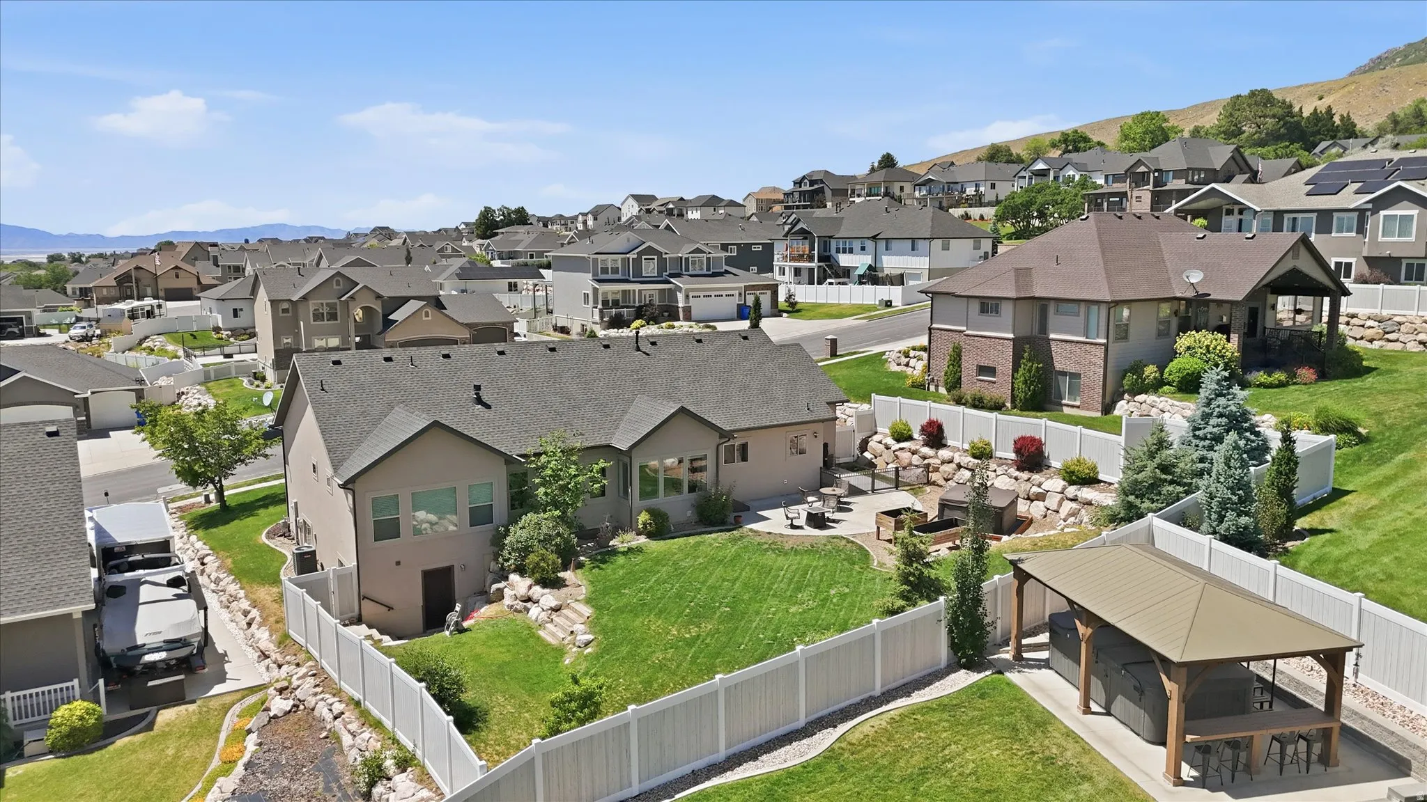 Expansive property featuring a manicured lawn, a paved patio with a built-in fire pit, terraced landscaping with rock retaining walls, and a dedicated outdoor pavilion
