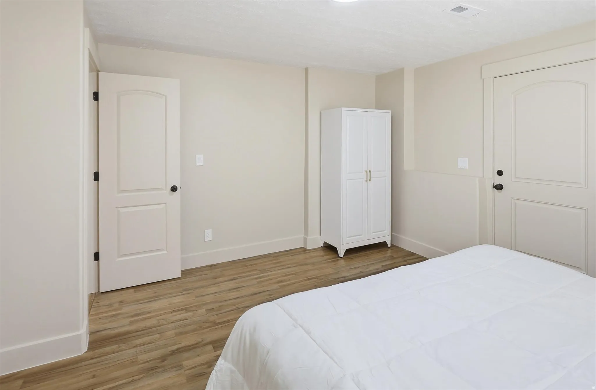 Interior room featuring wood-finish flooring, light neutral wall tones, white baseboards, and white paneled doors with black hardware