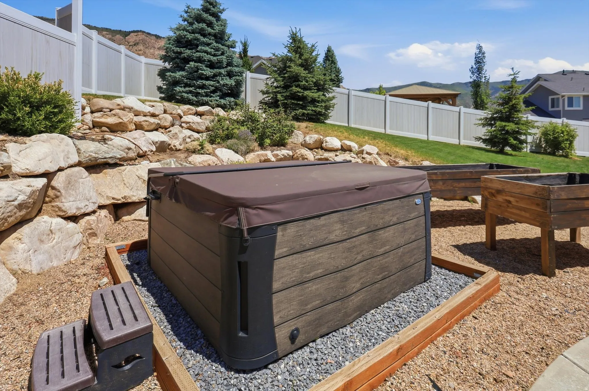 Outdoor spa with cover, framed by a gravel bed and wood border
