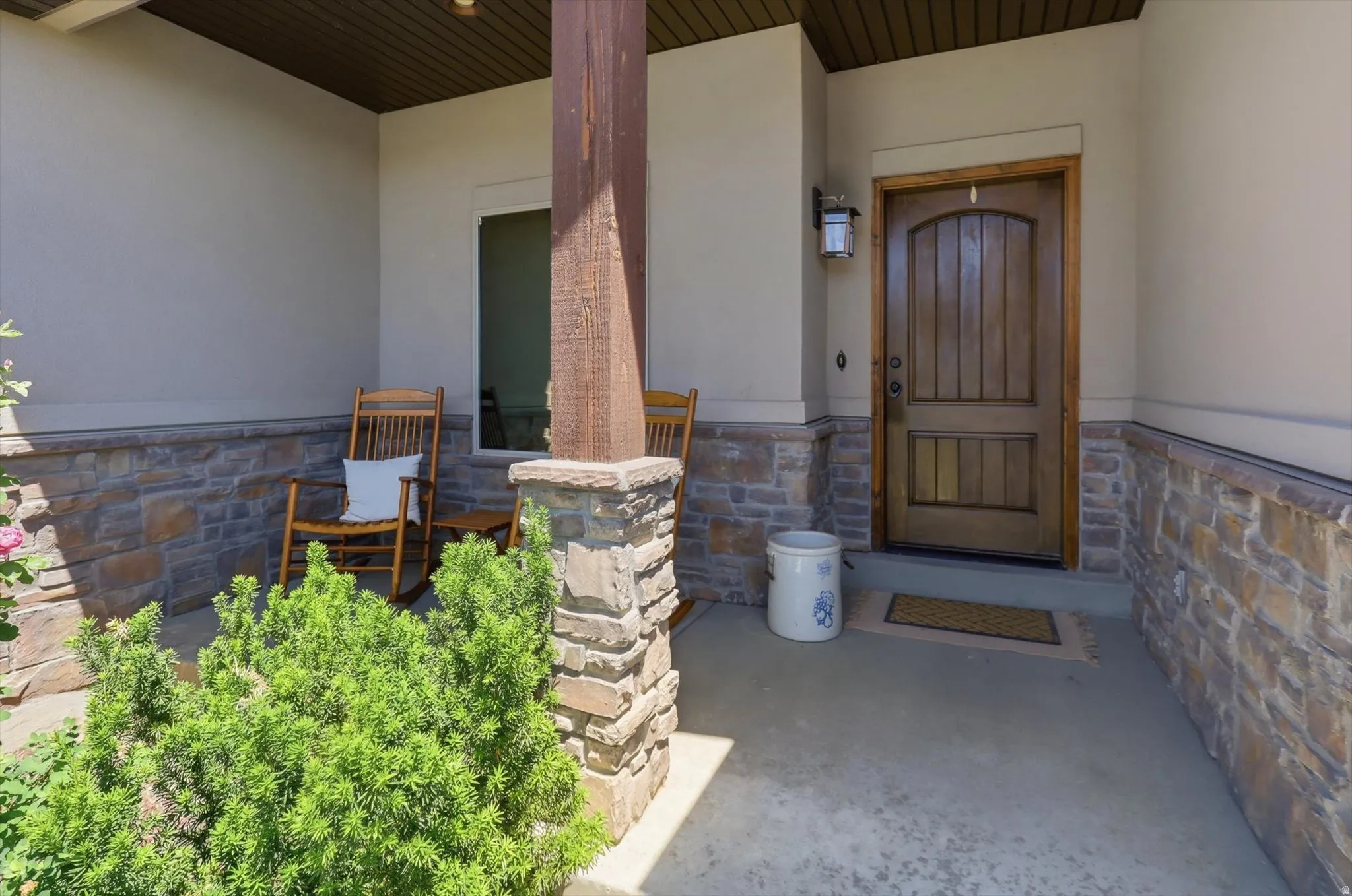 Covered front porch featuring a wood-panel entry door, stone wainscoting, and a wood beam accent