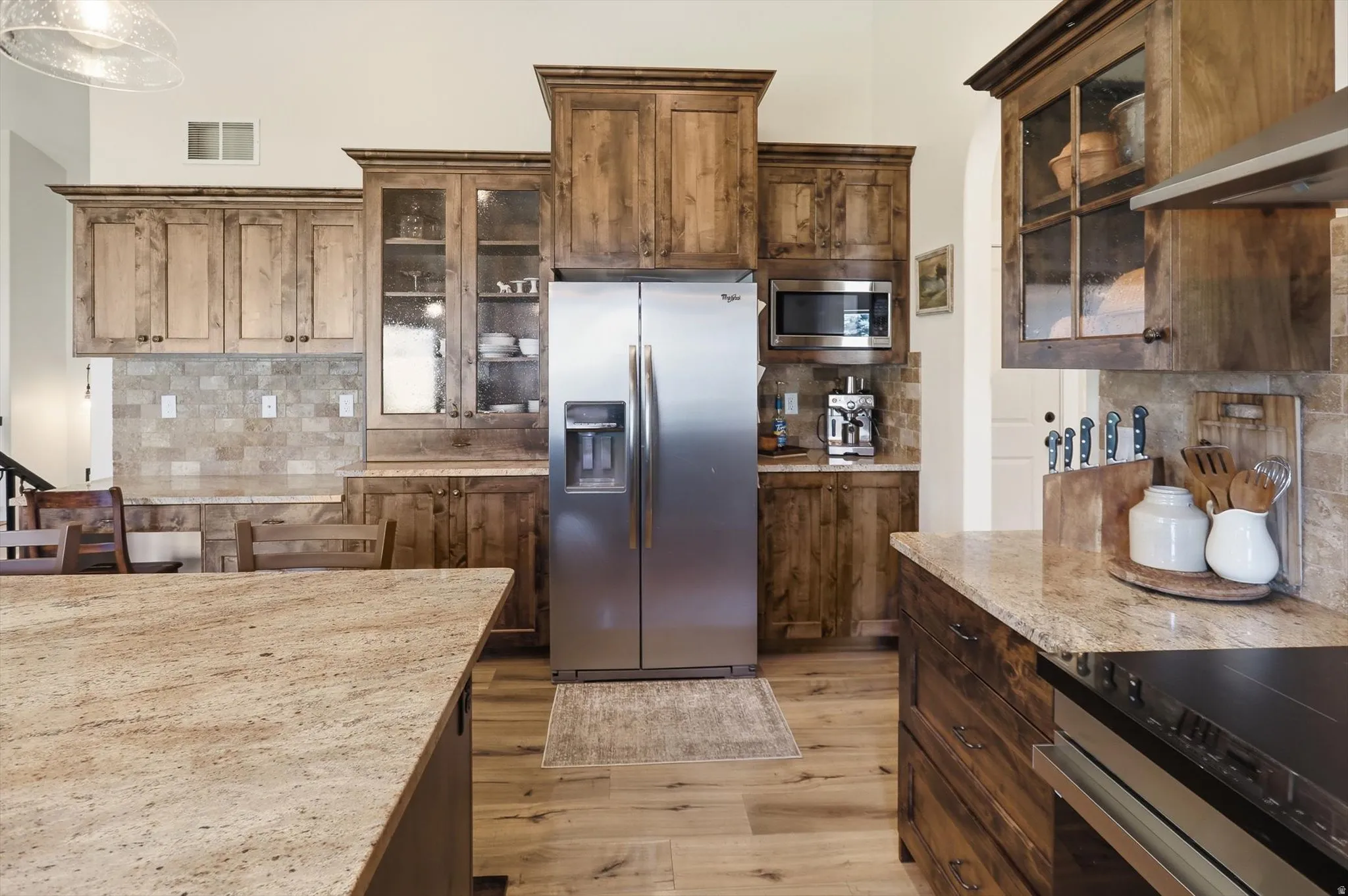 Kitchen featuring wood-finish cabinetry, stainless steel appliances, speckled stone countertops, and a tile backsplash