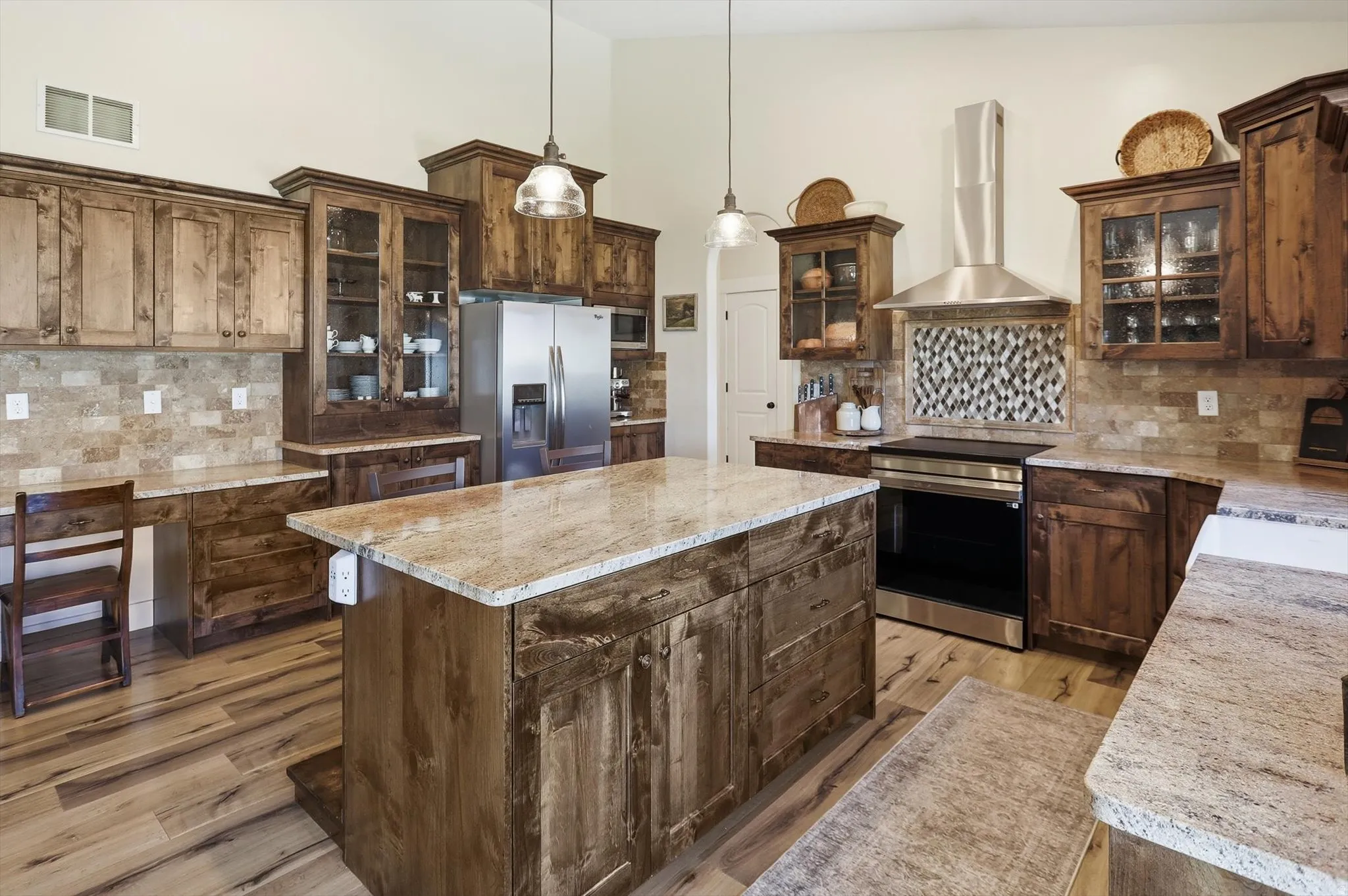 Gourmet kitchen featuring a large central island, light-toned granite countertops, stainless steel appliances, custom wood cabinetry, and wood-finish flooring