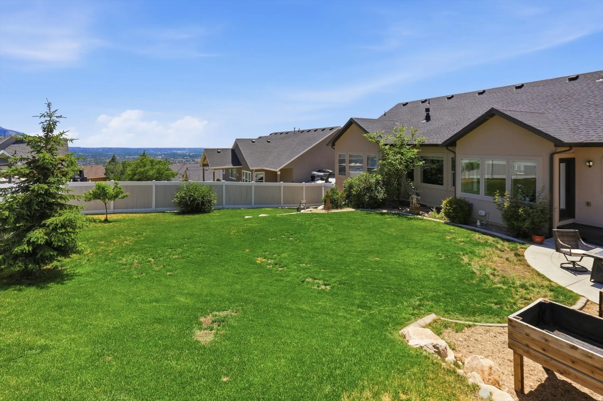 Expansive backyard featuring a manicured lawn, a concrete patio, a privacy fence, established shrubbery, and a raised planter box