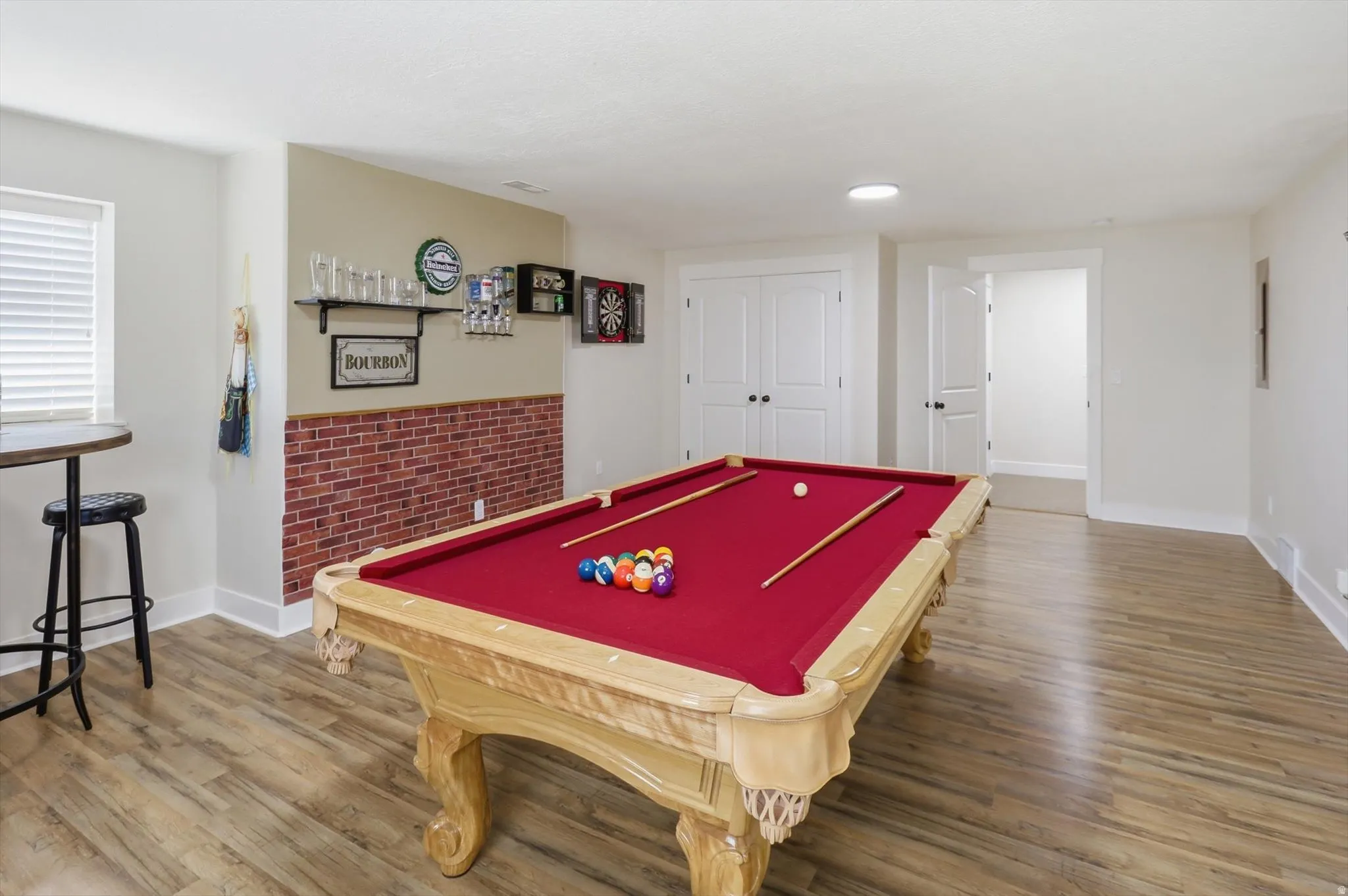 Recreation area featuring wood-finish flooring, a decorative brick-effect wall, and recessed ceiling lighting