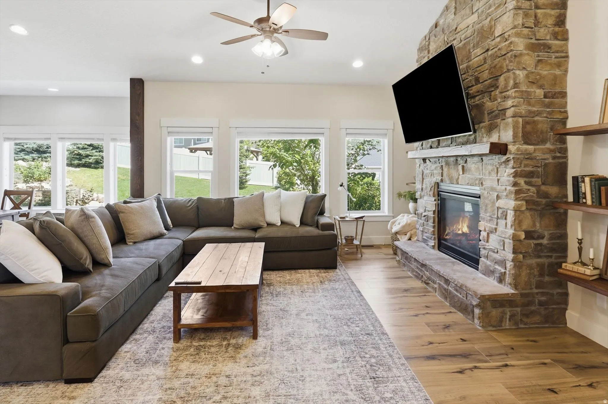Spacious living area featuring a floor-to-ceiling stone fireplace, wood-finish flooring, and multiple windows