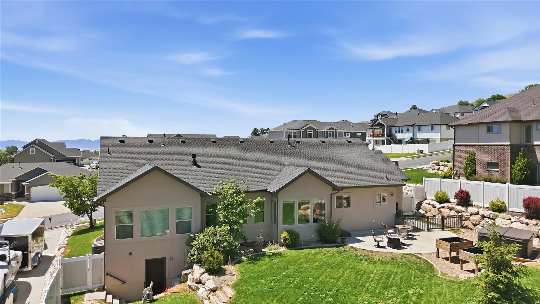 Rear exterior featuring a large concrete patio, terraced landscaping with rock accents, mature shrubs, and a fenced perimeter