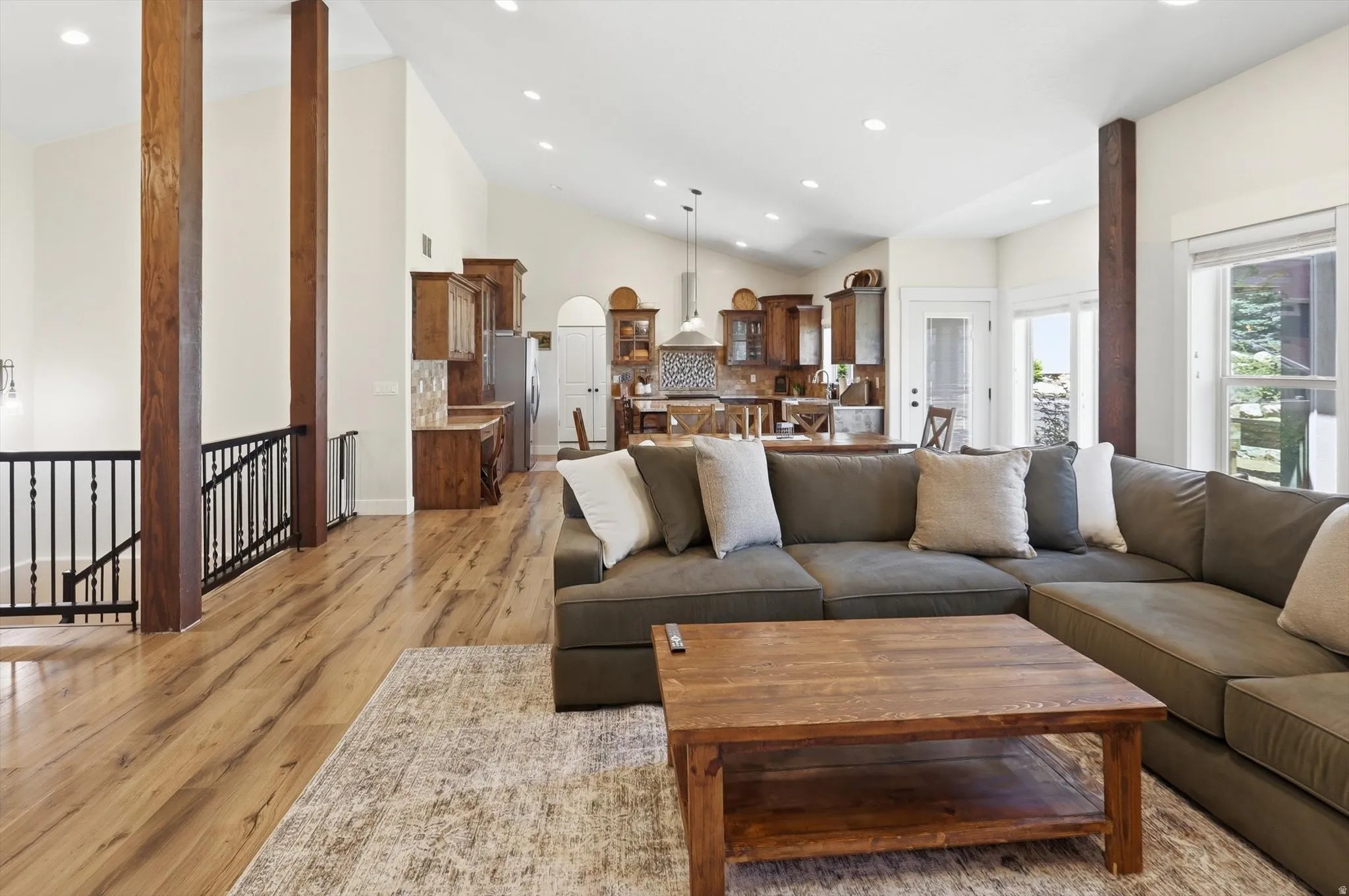 Open concept living area featuring vaulted ceilings, wood-finish flooring, recessed lighting, exposed structural beams, and a black wrought iron railing