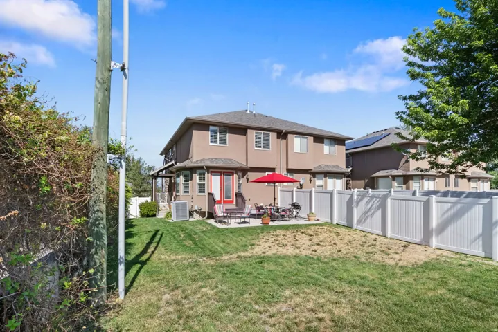 Rear exterior featuring a patio, manicured lawn, full privacy fencing, and an upper-level covered porch