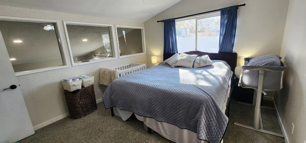 Carpeted room with vaulted ceiling and a large window featuring blue drapery