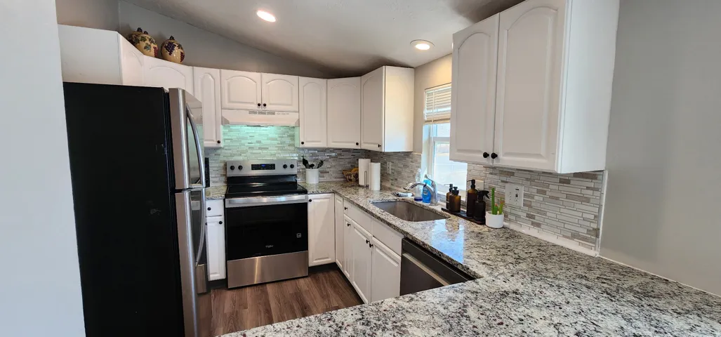 Kitchen featuring granite-style countertops, white cabinetry with black hardware, stainless steel appliances, and wood-finish flooring