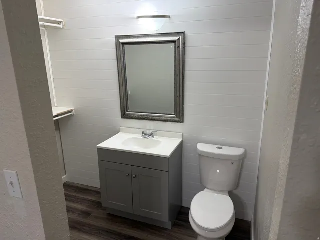 Bathroom featuring shiplap-style wall paneling, a single vanity with a white countertop, and wood-finish flooring