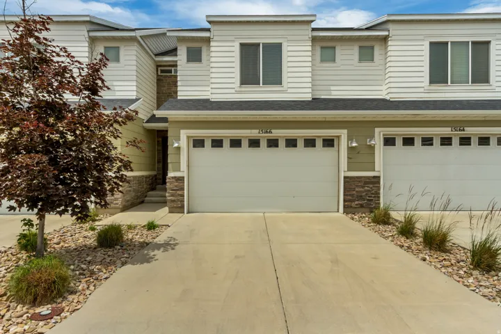 Contemporary multi-level townhome featuring a two-car attached garage, stone accents, and light-toned horizontal siding