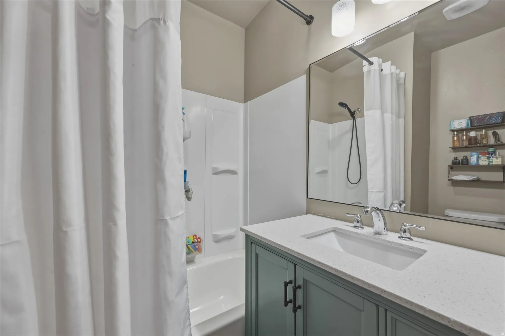 Bathroom featuring a built-in tub with a white surround, a teal vanity cabinet with dark hardware, a white countertop with an integrated sink, and a large wall-mounted mirror