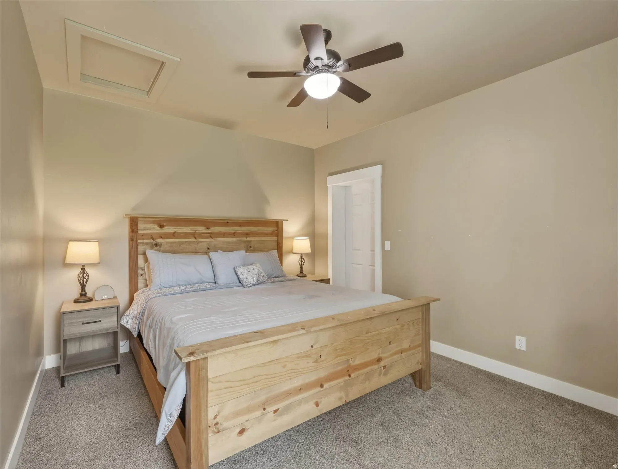Bedroom 1.   Carpeted room featuring a sloped ceiling with an attic access panel, a ceiling fan with integrated lighting, and white trim molding