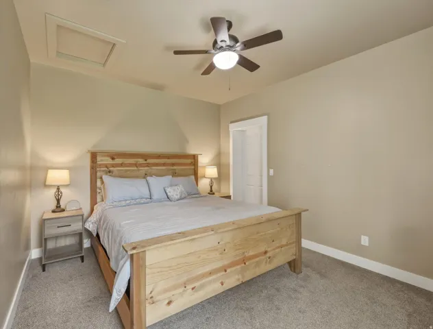 Bedroom 1.   Carpeted room featuring a sloped ceiling with an attic access panel, a ceiling fan with integrated lighting, and white trim molding