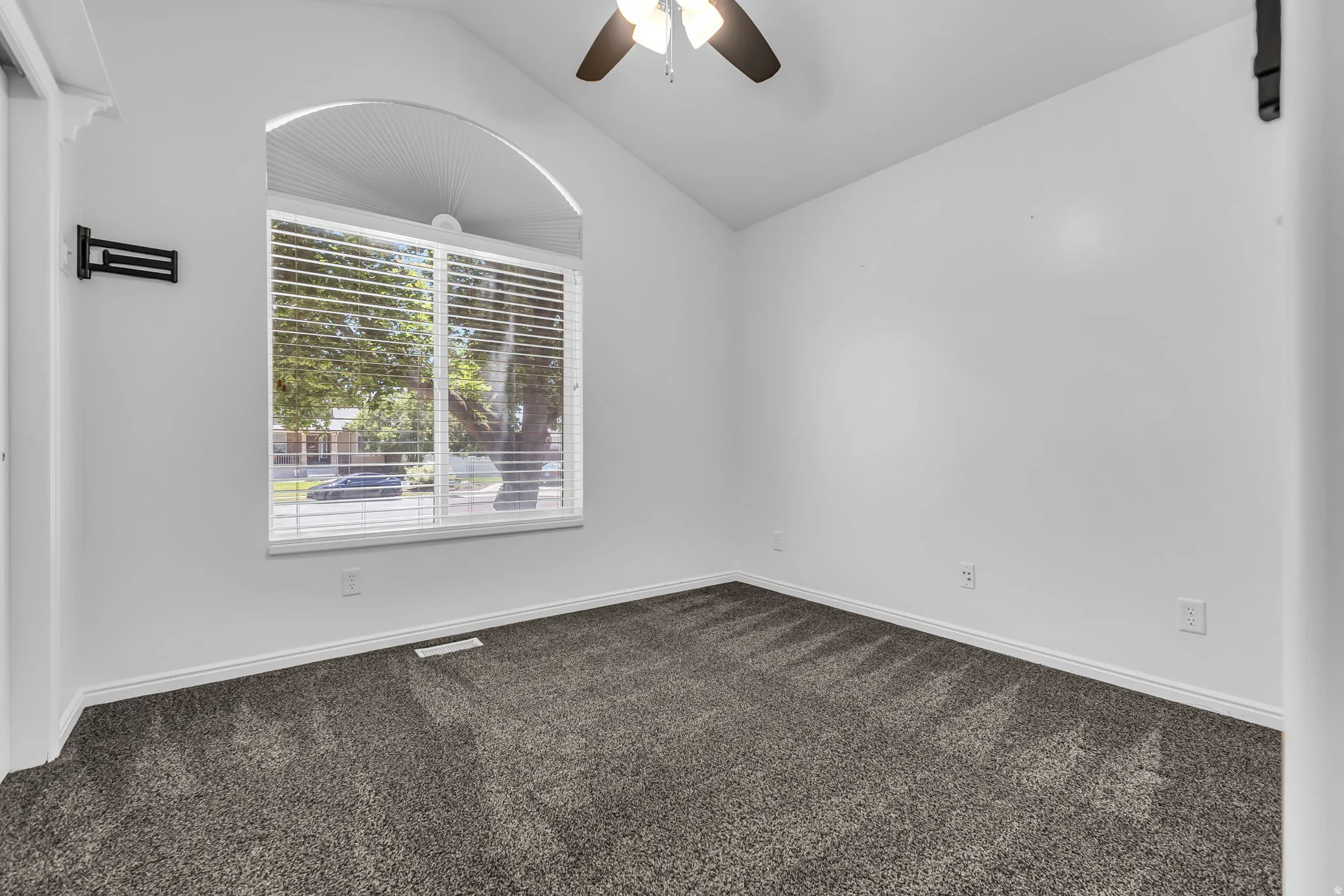 Vaulted ceiling room with an arched window featuring horizontal blinds