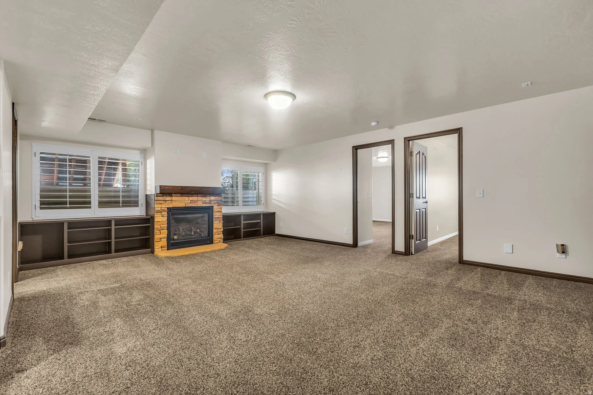 Spacious room featuring broadloom carpet flooring, a stone-clad fireplace with a wood-finish mantel, and built-in shelving units