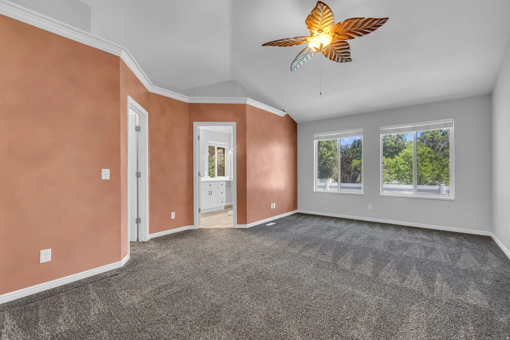 Spacious room featuring vaulted ceilings, a decorative ceiling fan, wall-to-wall carpeting, and multiple windows