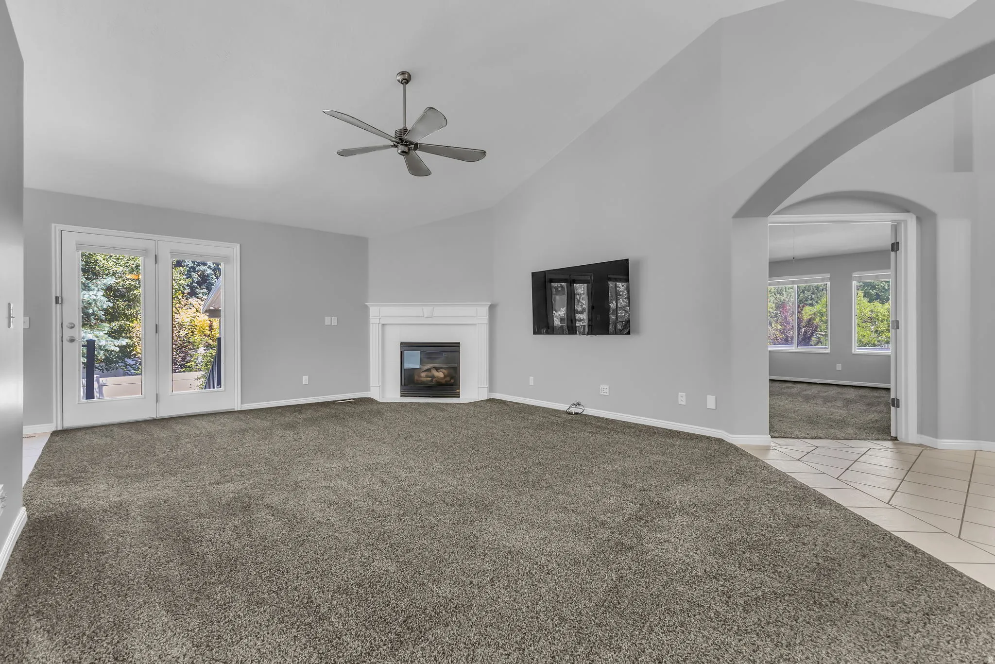 Spacious main living area featuring vaulted ceilings, a corner fireplace with a white mantel and opening to the deck and patio.