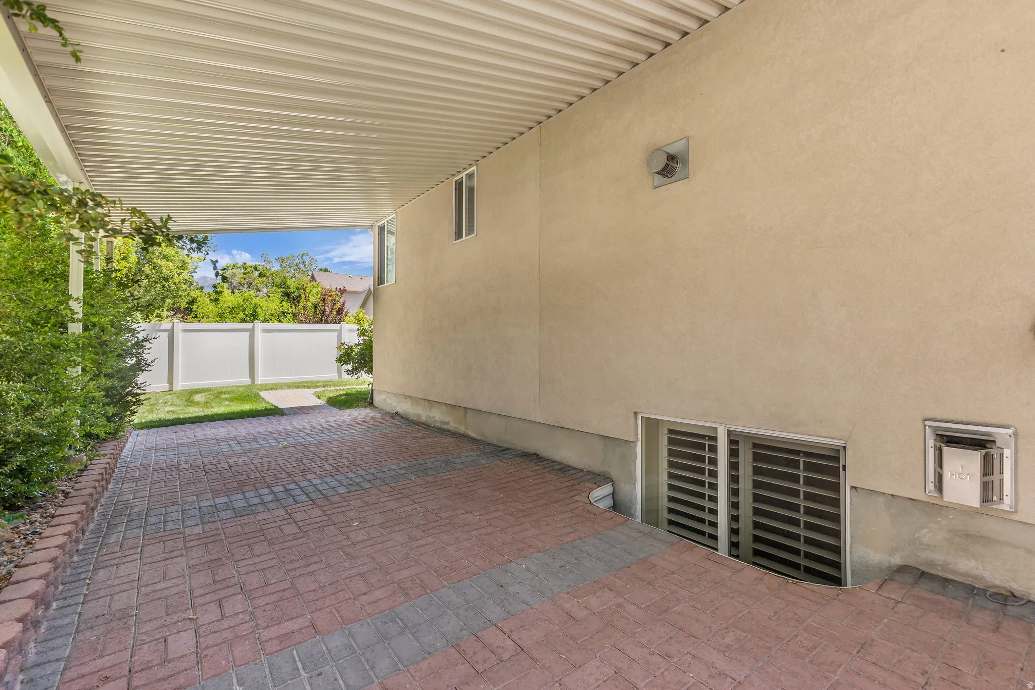 Covered patio featuring an open-gable roof, brick pavers, stucco exterior, and basement window wells