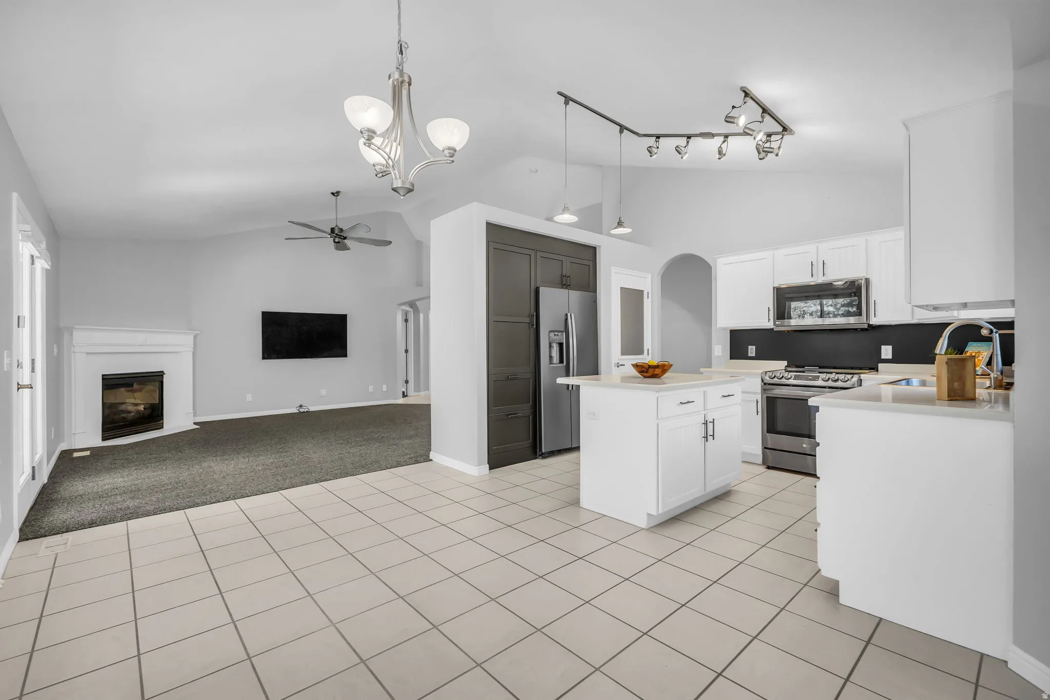Open-concept kitchen featuring an island with a breakfast bar, white cabinetry, stainless steel appliances, and tile flooring