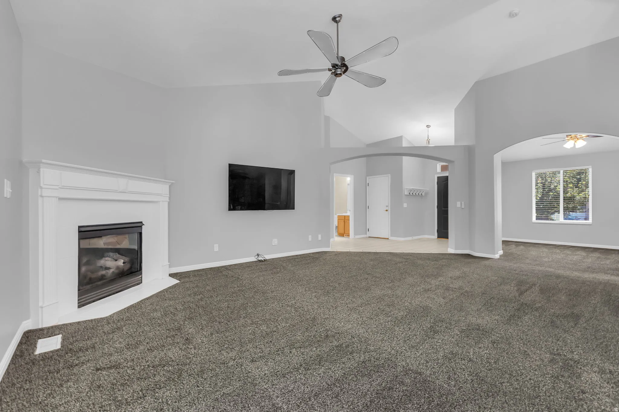 Spacious living area featuring a corner fireplace with a white mantel, vaulted ceilings, and a ceiling fan
