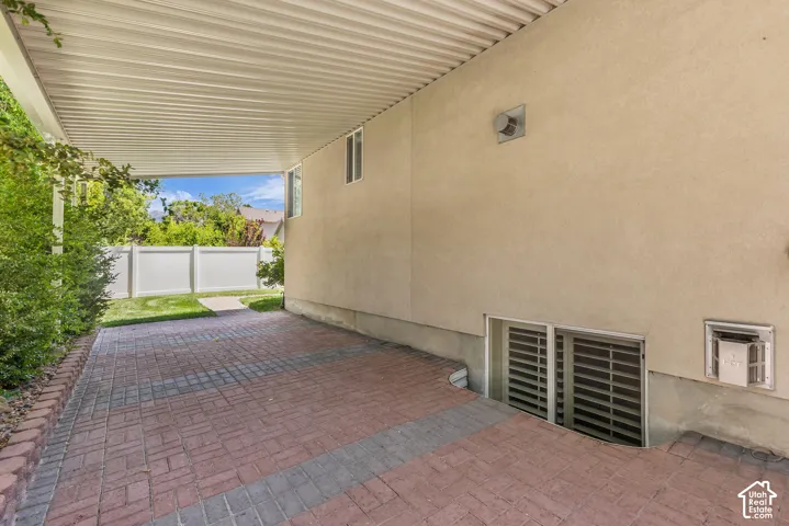 Covered patio featuring an open-gable roof, brick pavers, stucco exterior, and basement window wells