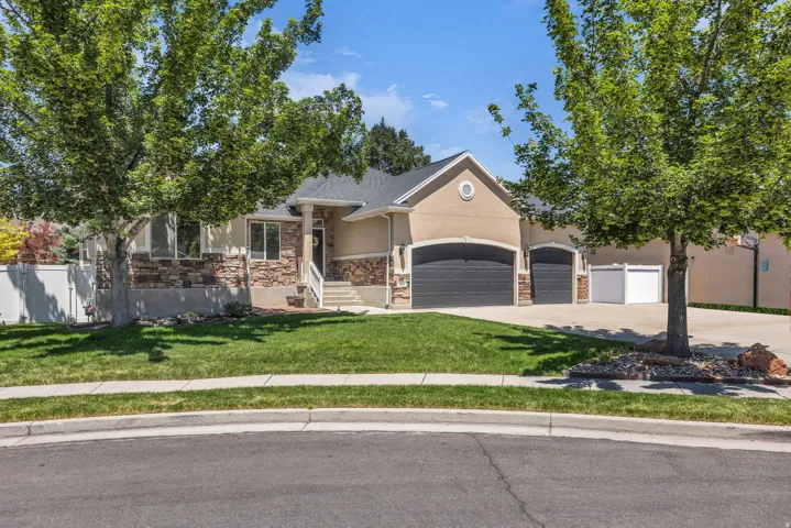 Front exterior featuring a stucco and stone facade, mature trees, a manicured lawn, a three-car garage, and a covered front porch.