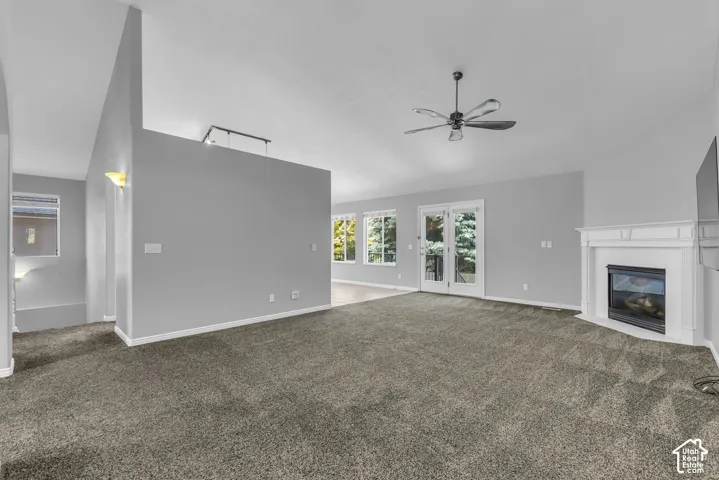 Spacious living area featuring vaulted ceilings, a ceiling fan, a corner fireplace with a white mantel, and double French doors opening to the deck.