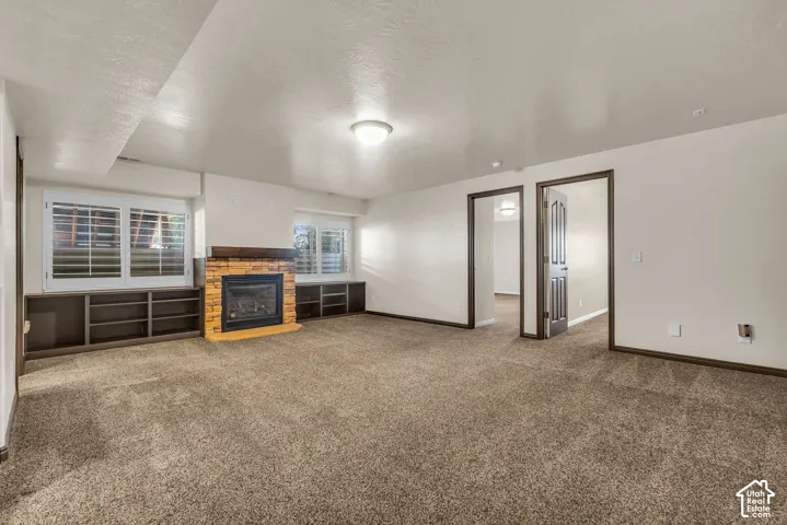 Spacious room featuring broadloom carpet flooring, a stone-clad fireplace with a wood-finish mantel, and built-in shelving units