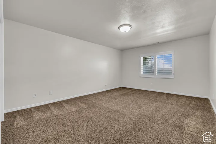 Spacious room featuring neutral wall tones, brown textured carpeting, and white baseboards