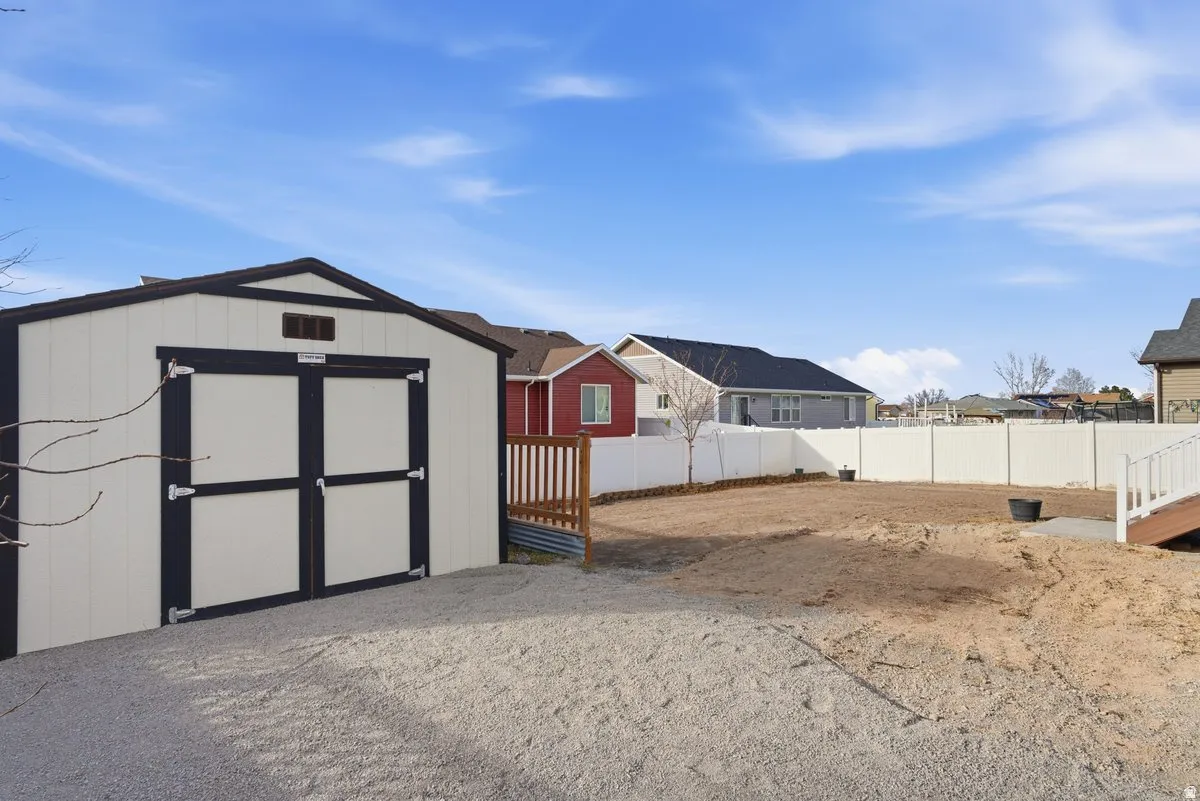 Spacious backyard featuring a storage shed with double doors, gravel ground cover, and a white privacy fence