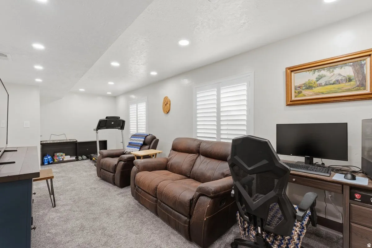 Spacious recreational room featuring recessed lighting, light gray carpet flooring, and white window shutters