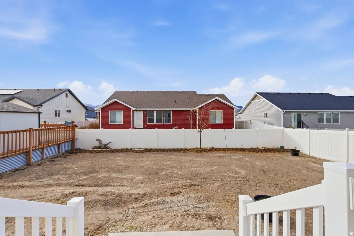 Expansive backyard with a level dirt surface, enclosed by white vinyl fencing and a wood-slat privacy fence