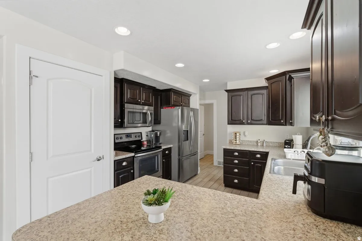 Kitchen featuring dark wood cabinetry, light-toned countertops, stainless steel appliances, recessed ceiling lighting, and wood-finish flooring
