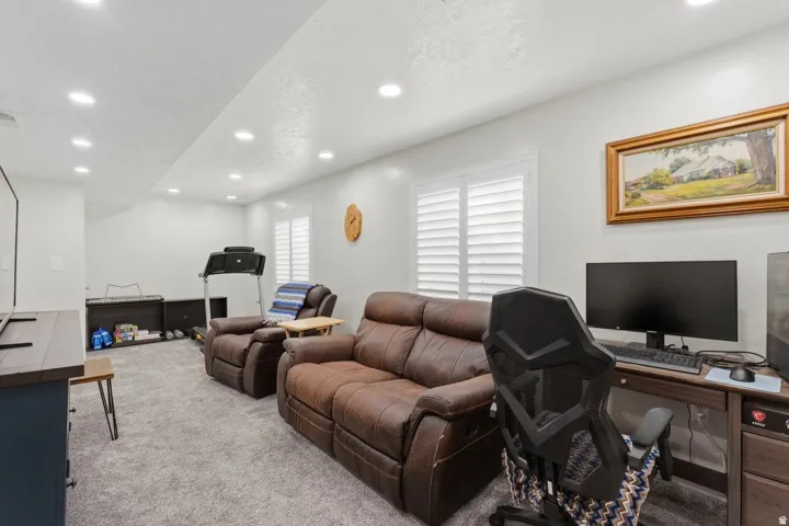 Spacious recreational room featuring recessed lighting, light gray carpet flooring, and white window shutters