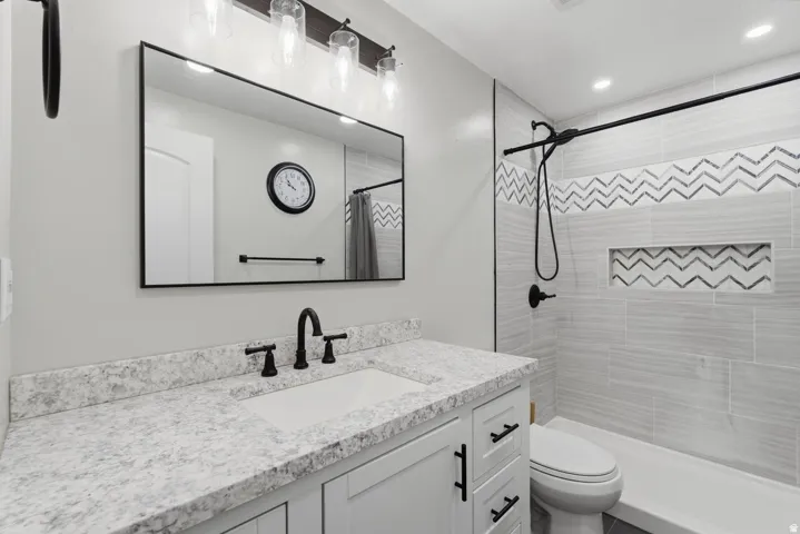 Bathroom featuring a white vanity with a speckled countertop, undermount sink, and matte black fixtures