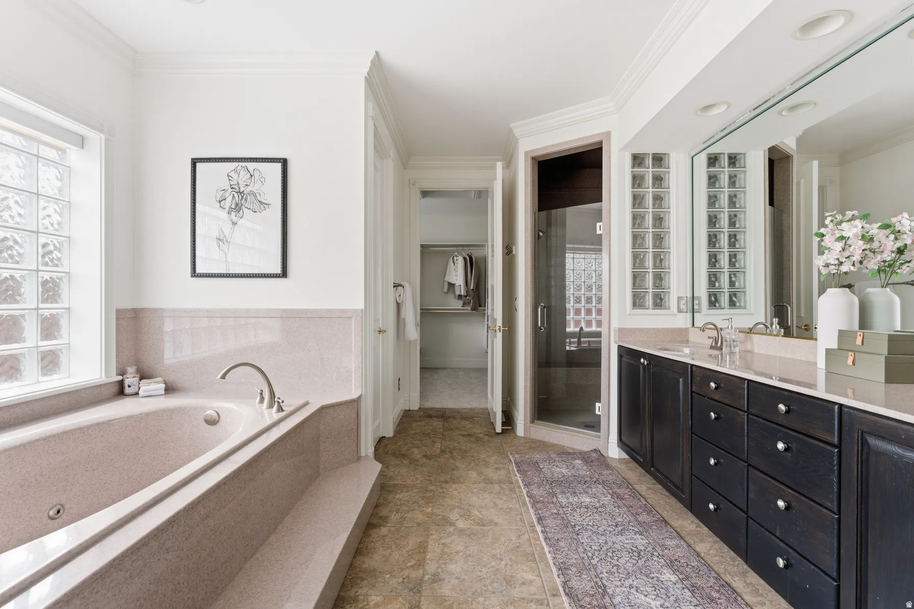 Bathroom featuring a built-in soaking tub, glass block window, dark wood-finish double vanity with dual sinks, and a glass-enclosed shower
