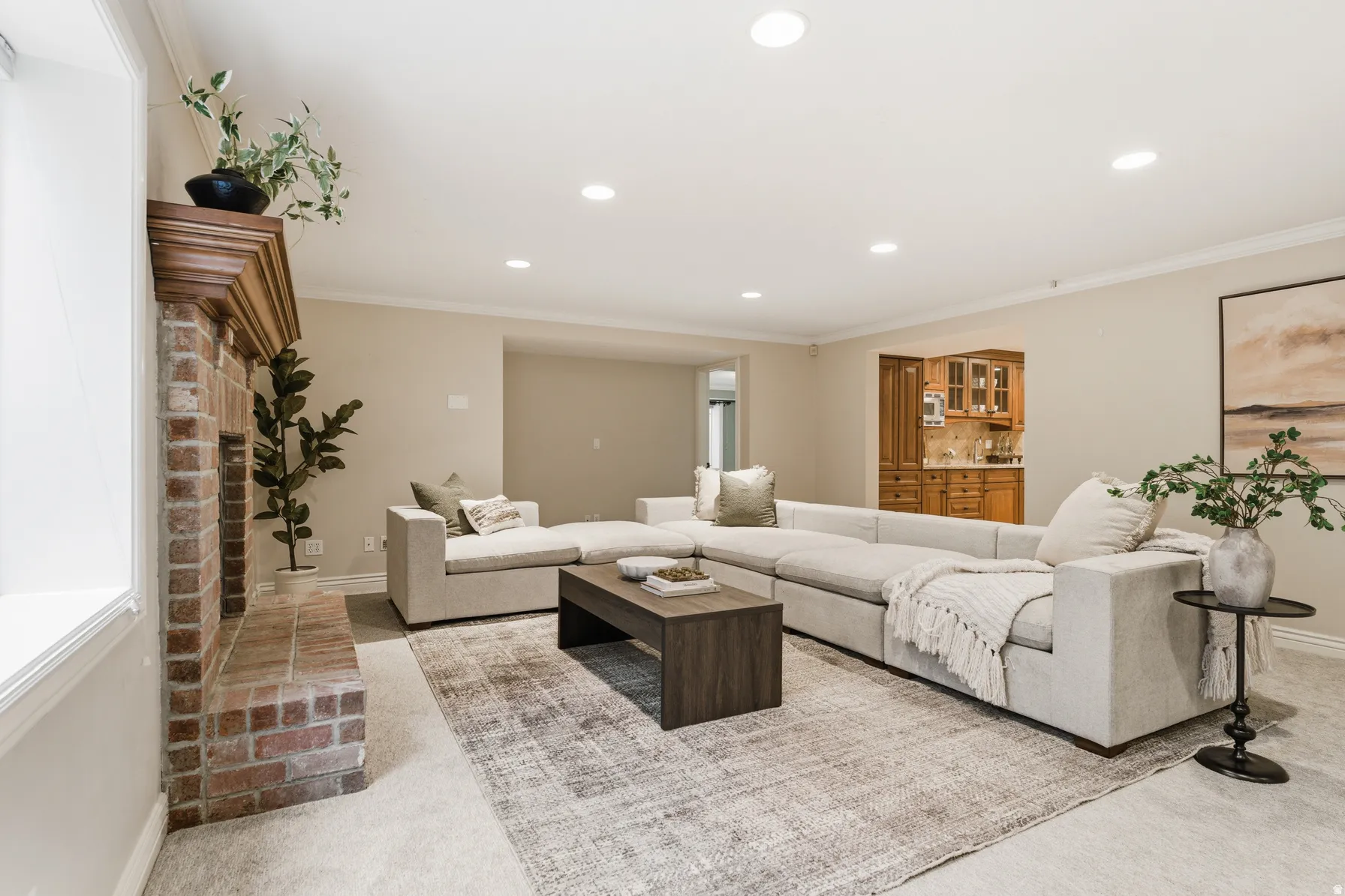 Spacious living area featuring a brick fireplace with a wood mantle, recessed lighting, crown molding, and neutral wall tones