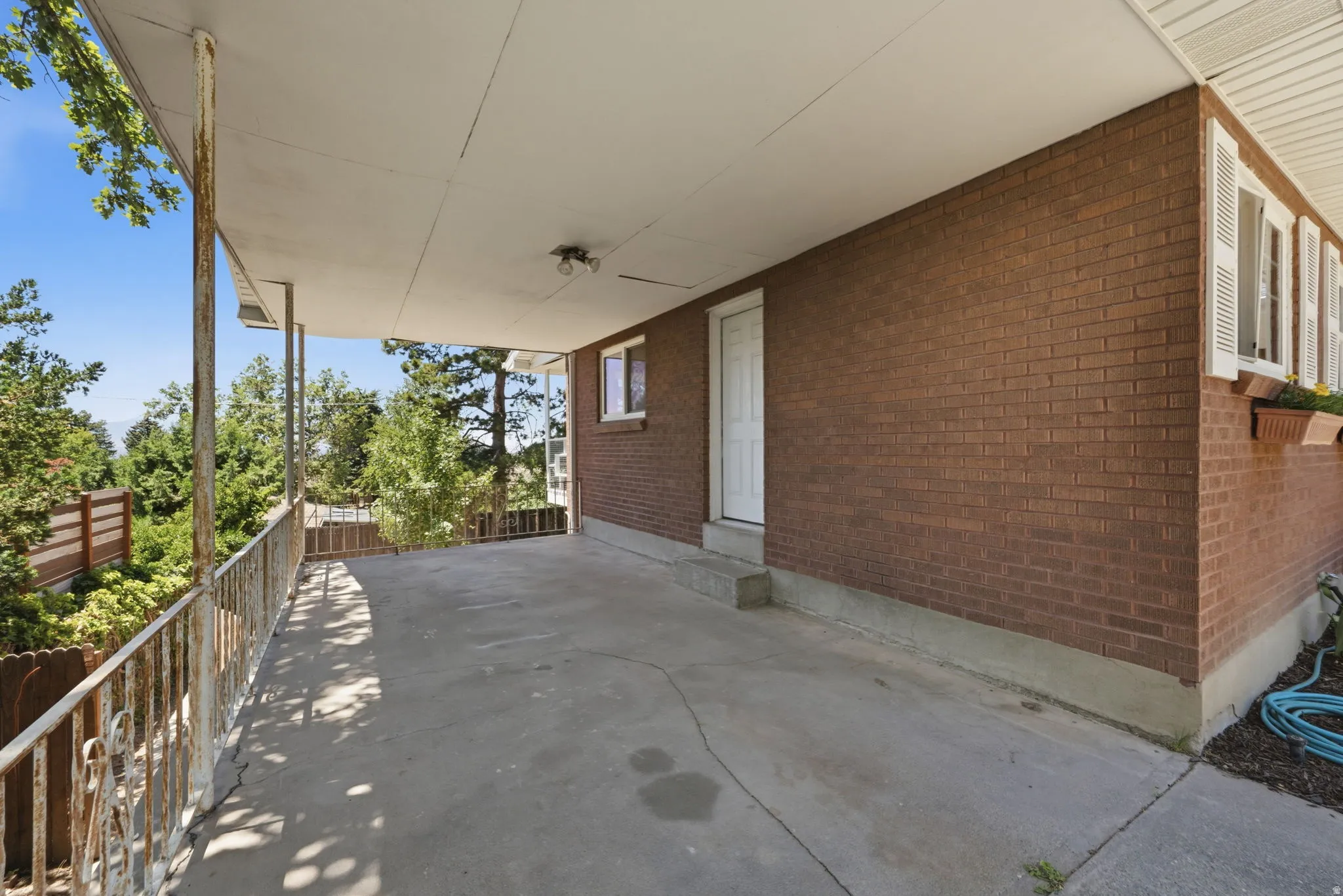 Covered patio with concrete flooring, brick exterior, white door, and white shuttered windows with flower boxes