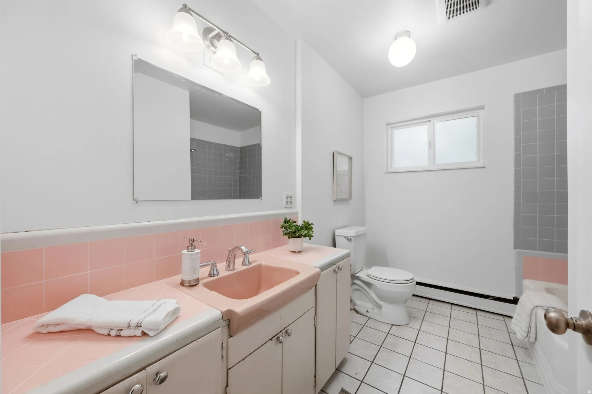 Bathroom featuring a tiled shower, white vanity with integrated pink sink, white toilet, and window