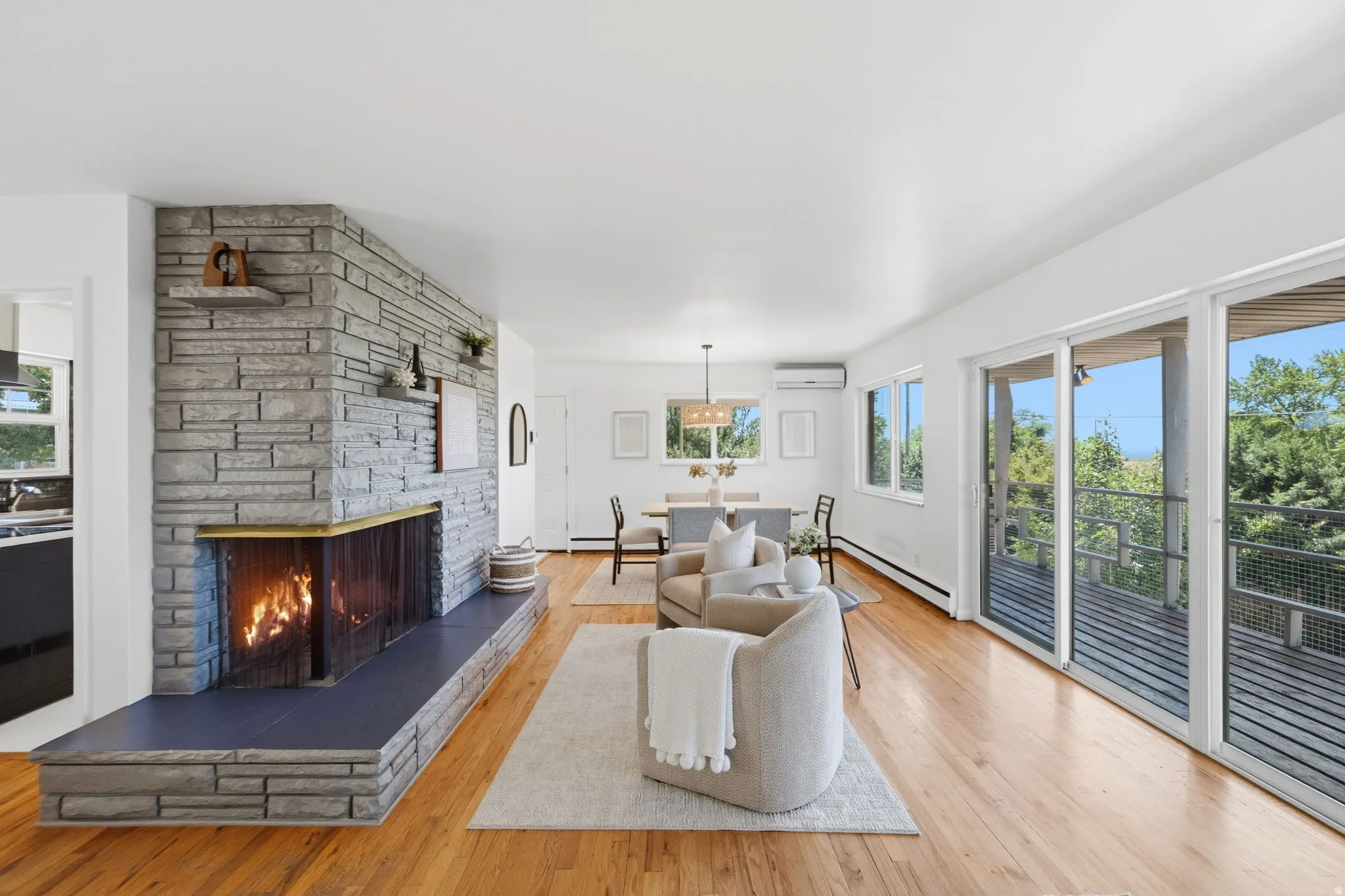 Expansive living area featuring a stone-clad fireplace with a hearth, wood-finish flooring, white walls, and multiple sliding glass doors opening to an outdoor deck