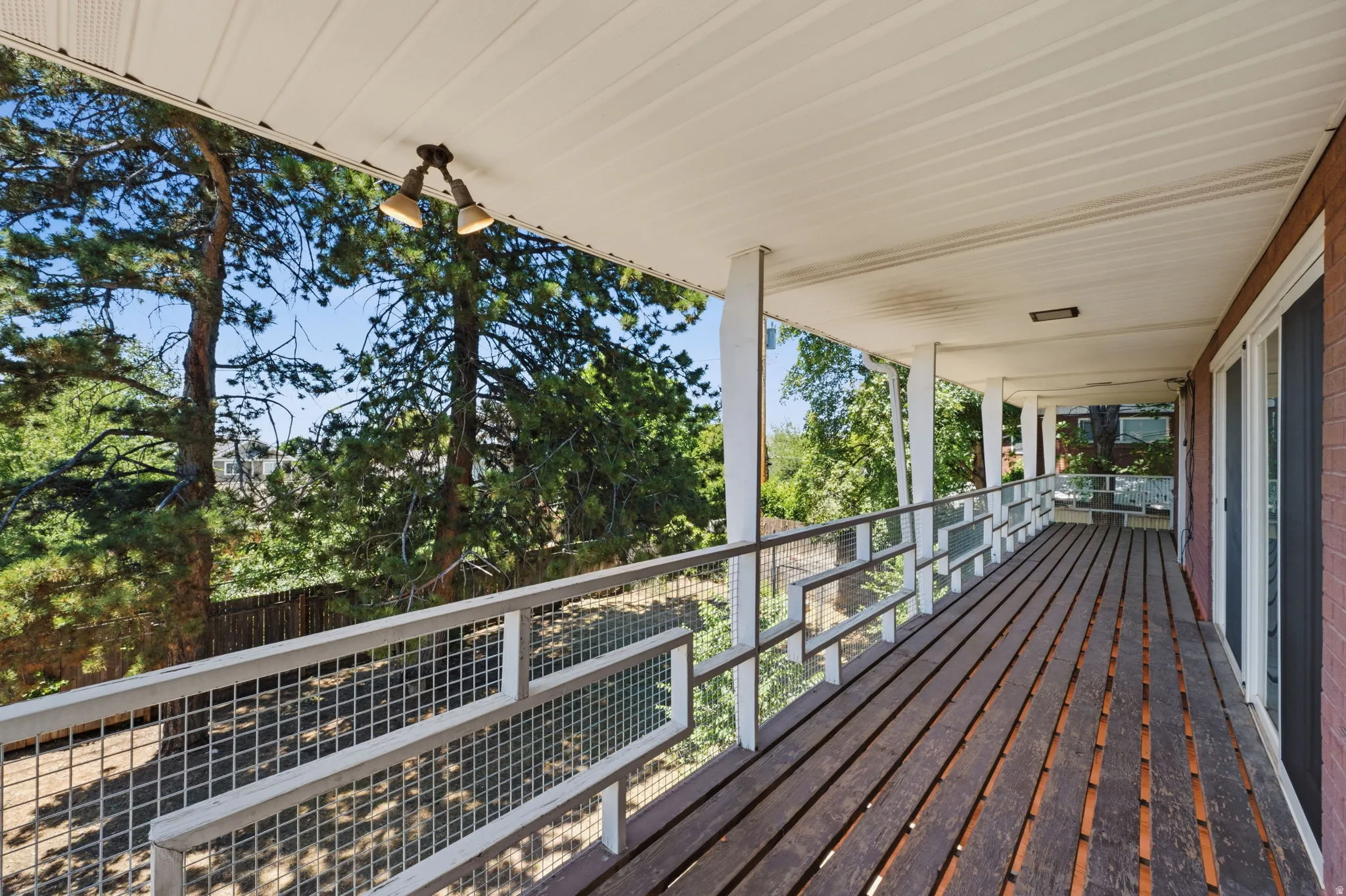 Expansive covered deck featuring wood plank flooring, white metal railings, and a white paneled ceiling with mounted lighting
